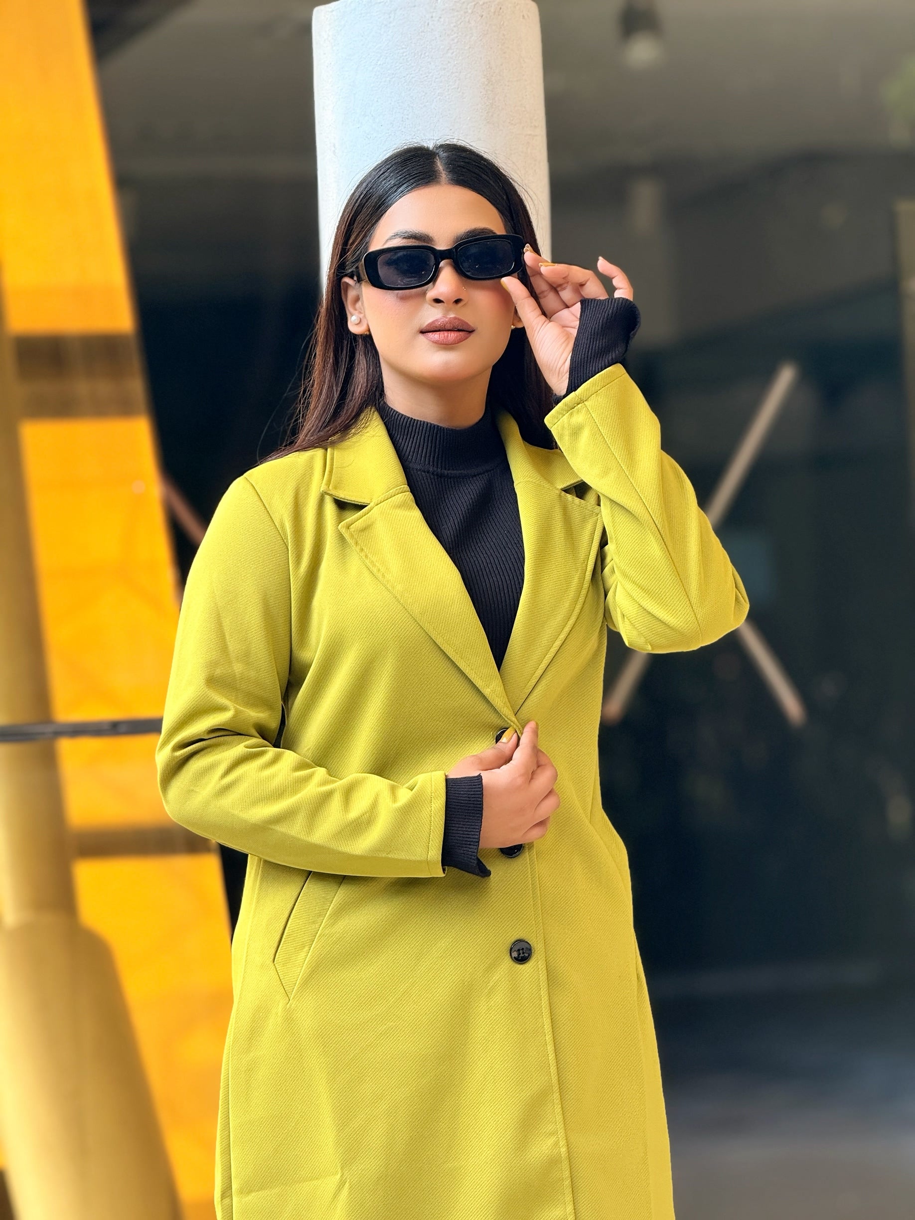 Woman wearing a bright yellow coat and sunglasses in an urban setting