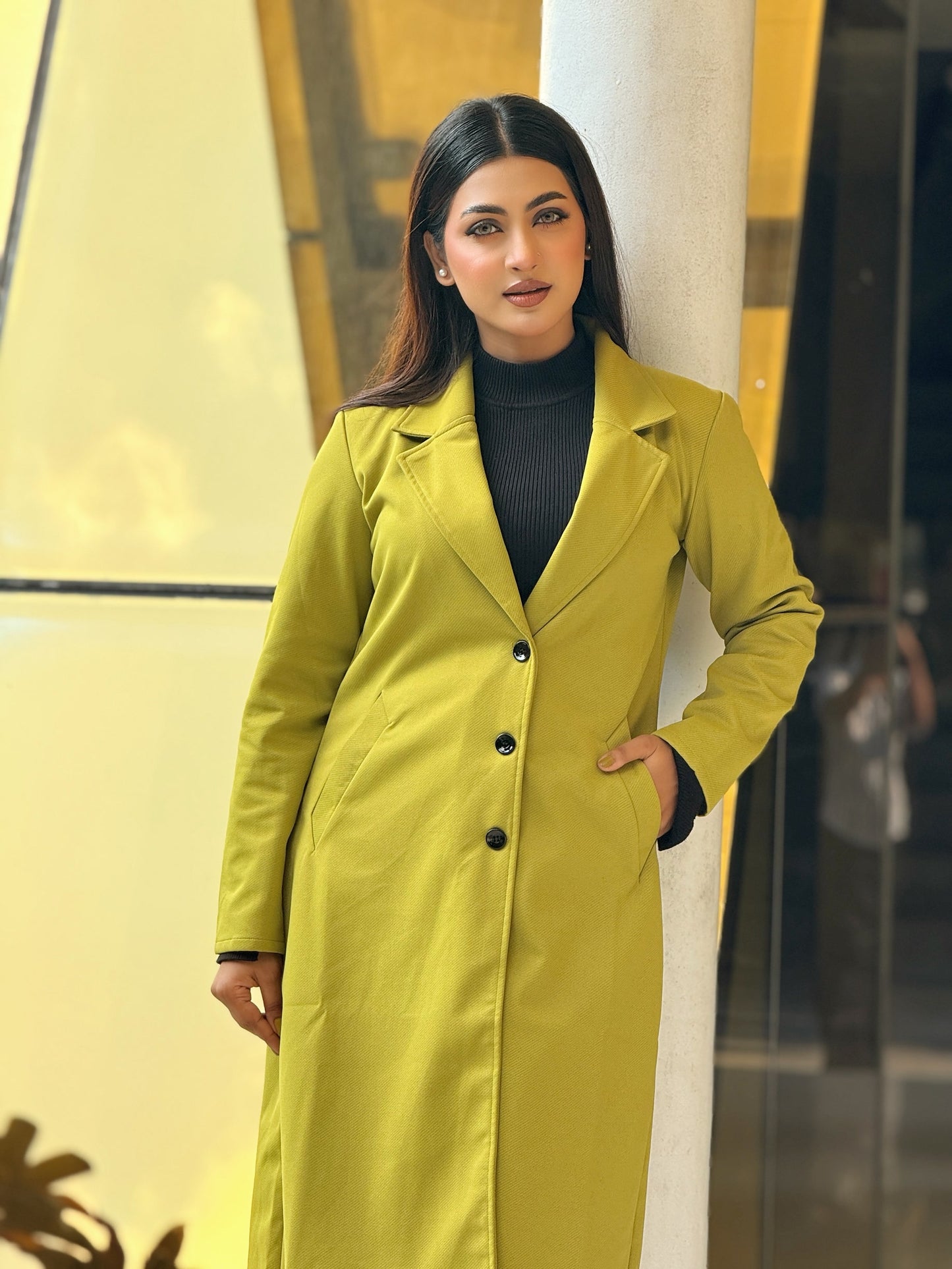Woman wearing a bright yellow coat standing against a yellow wall.