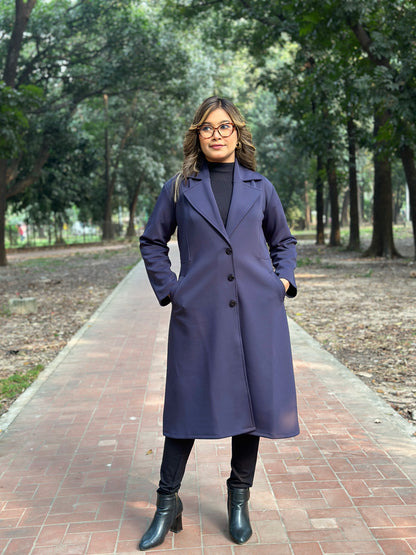 Woman wearing a long dark coat standing on a path with trees in the background