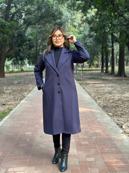 Woman wearing a long blueish black overcoat in a park setting