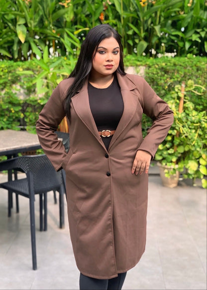 Woman wearing a brown coat standing outdoors with greenery in the background