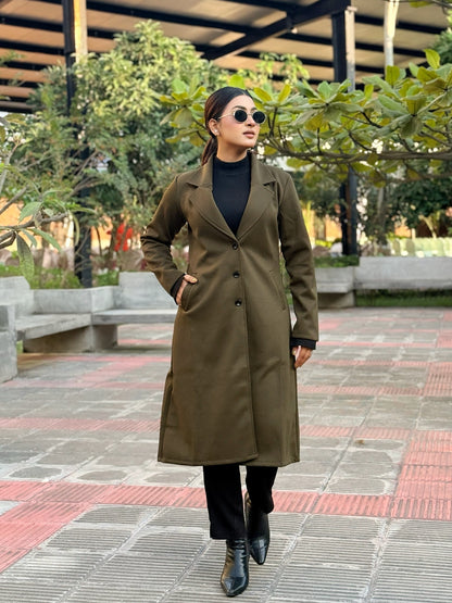 Person wearing a long olive green coat in an outdoor setting with trees and benches.