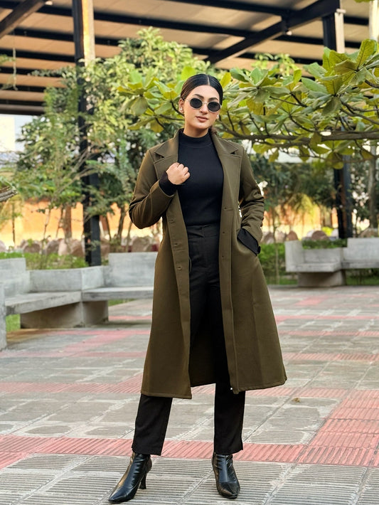 Woman in a long brown coat standing outdoors with trees and benches in the background