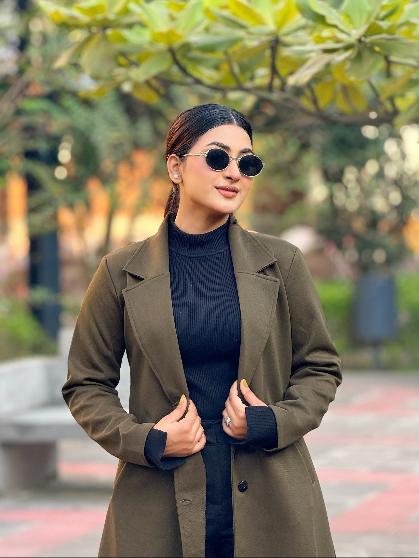 Woman wearing a green coat and black sunglasses outdoors with blurred background