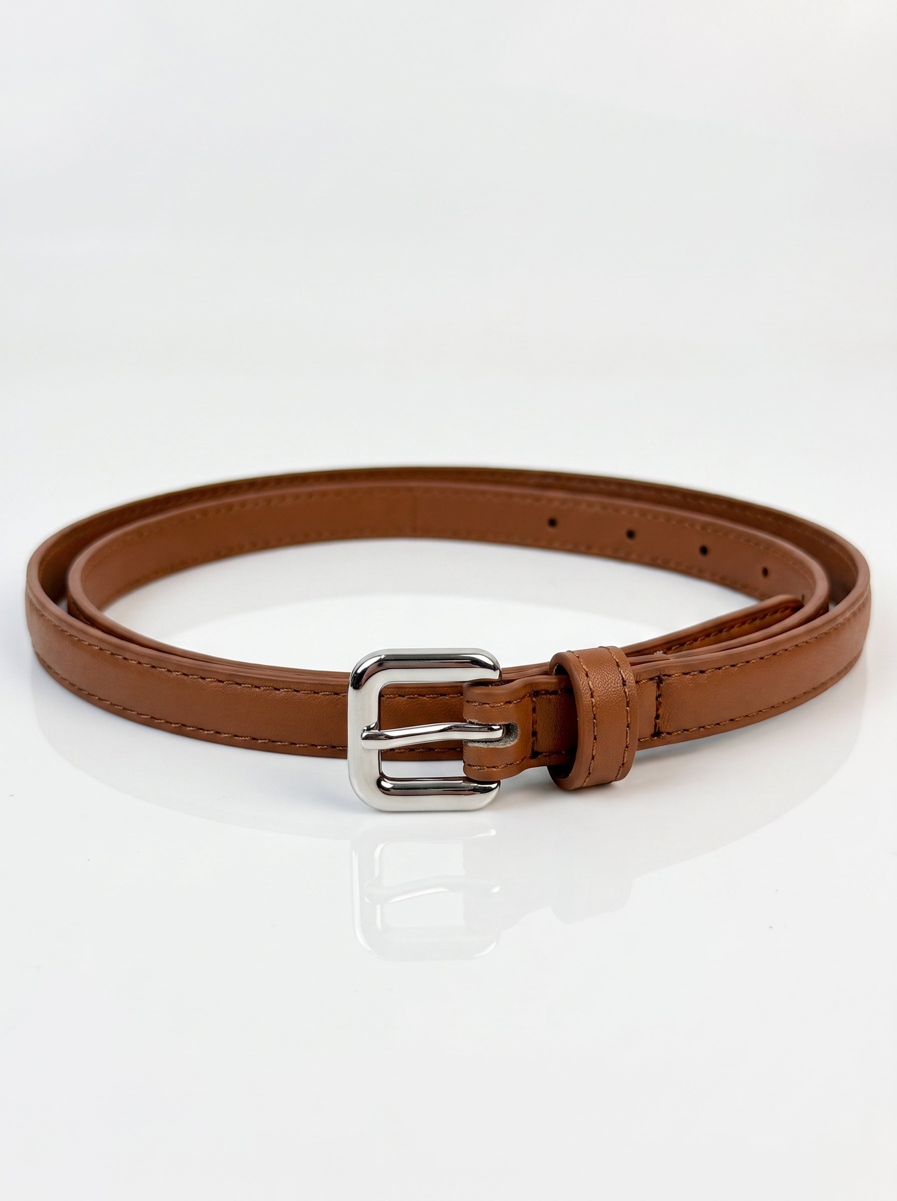 A brown faux leather belt with a silver-tone metal buckle, neatly coiled on a reflective white surface.