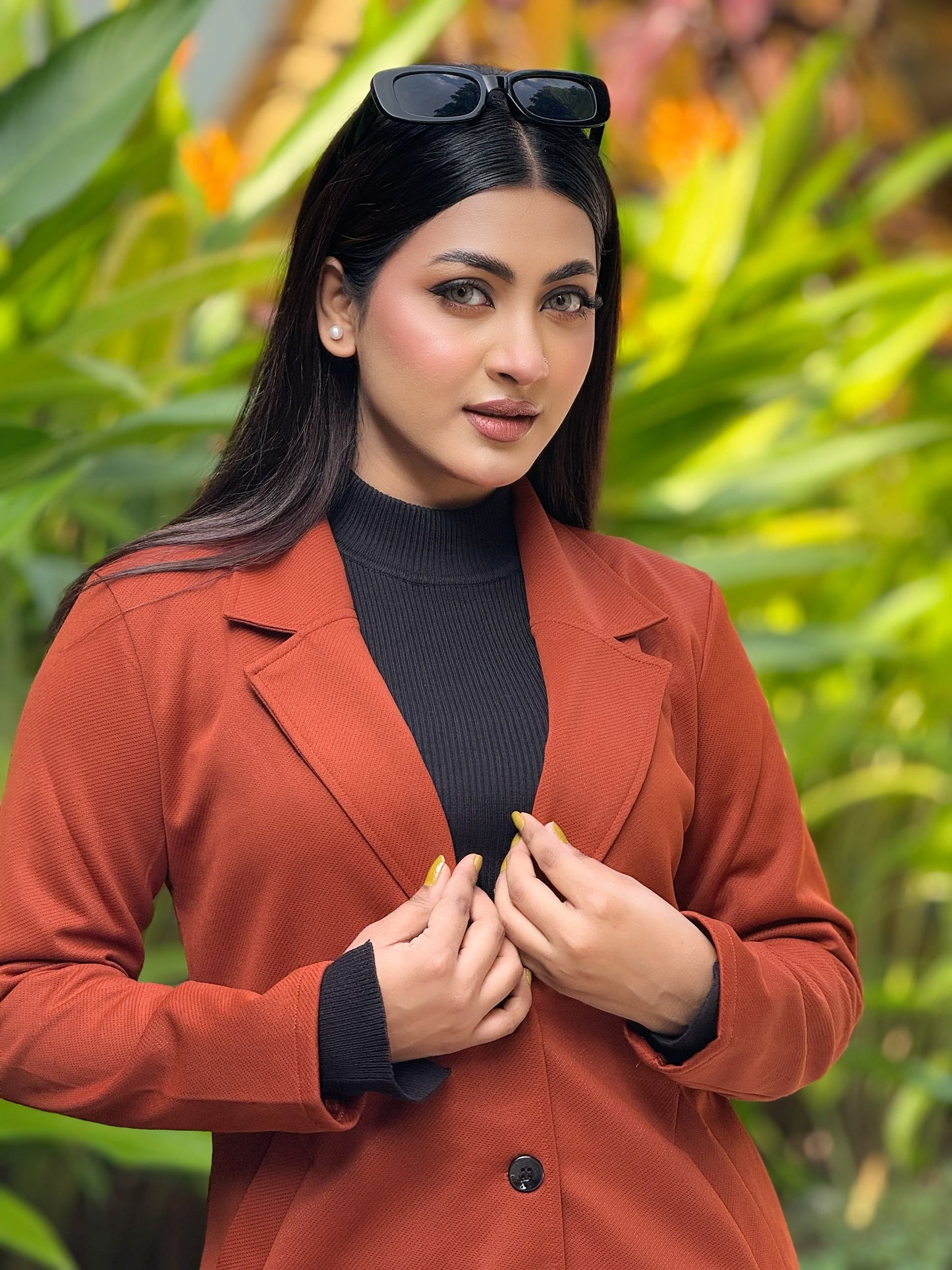Woman wearing a red coat and black sunglasses with a blurred green background