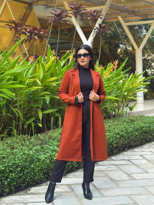 Woman in a red coat standing in front of a modern architectural structure with greenery.