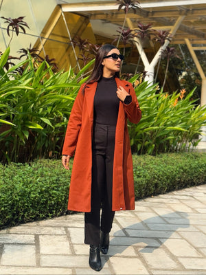 Woman in a red coat standing outdoors with greenery and a building in the background