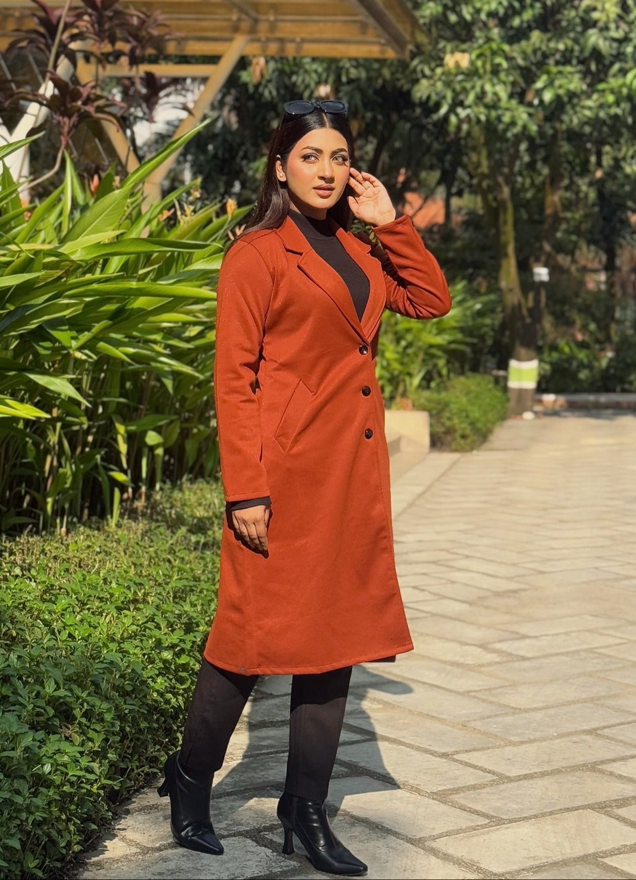 Woman in an orange coat standing on a pathway with greenery around