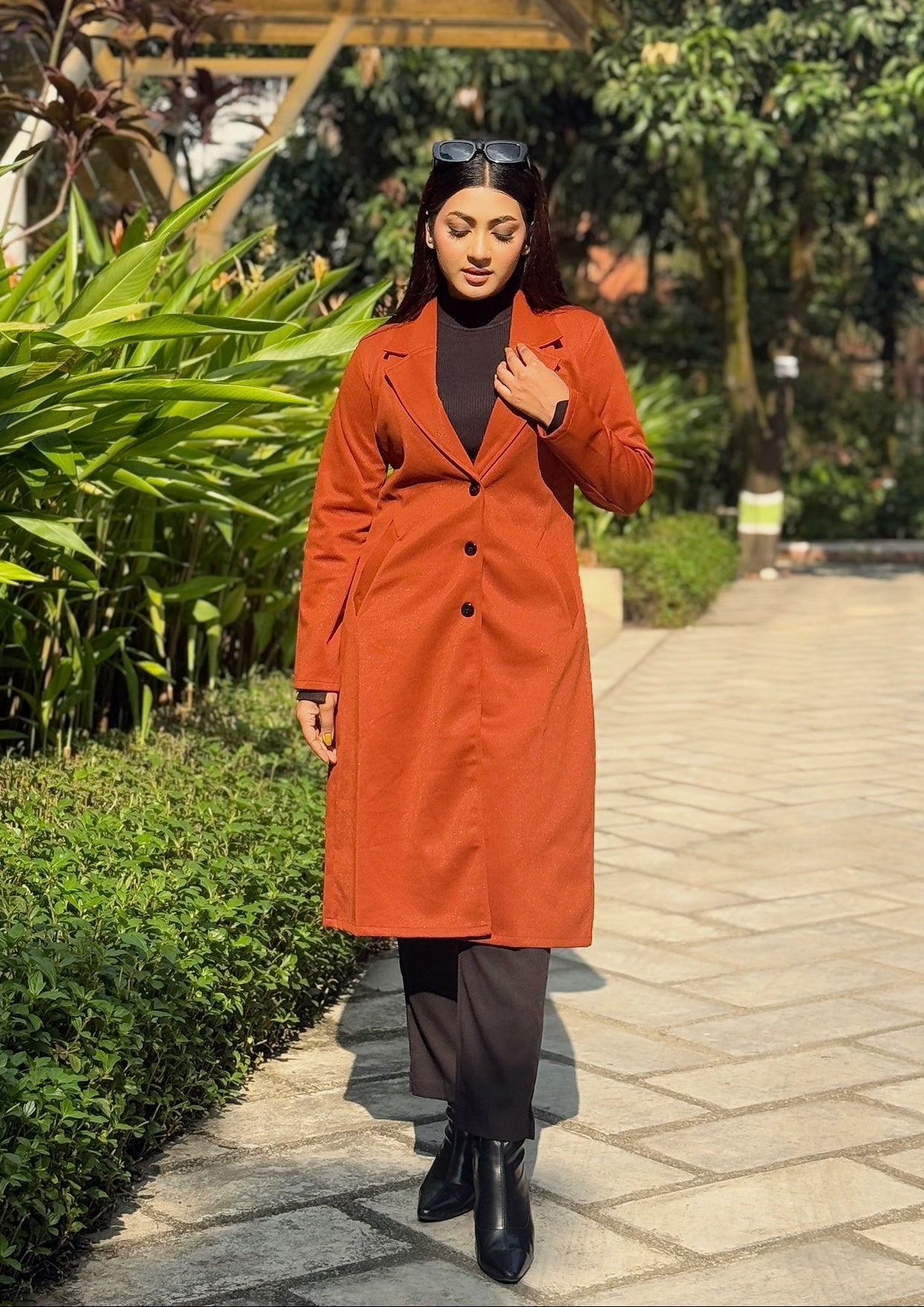 Woman in an orange coat standing on a paved path with greenery around
