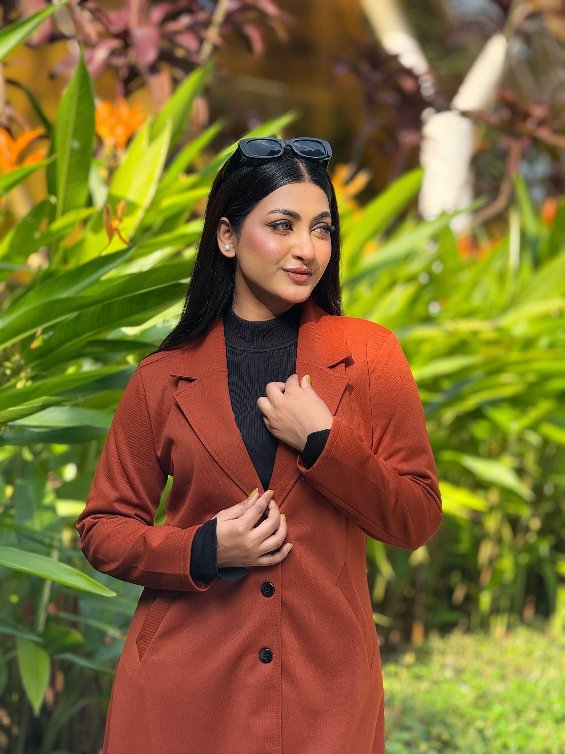 Woman in a red coat standing among green foliage
