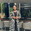 Woman wearing a zebra print long shrug in an outdoor setting with tables and chairs.