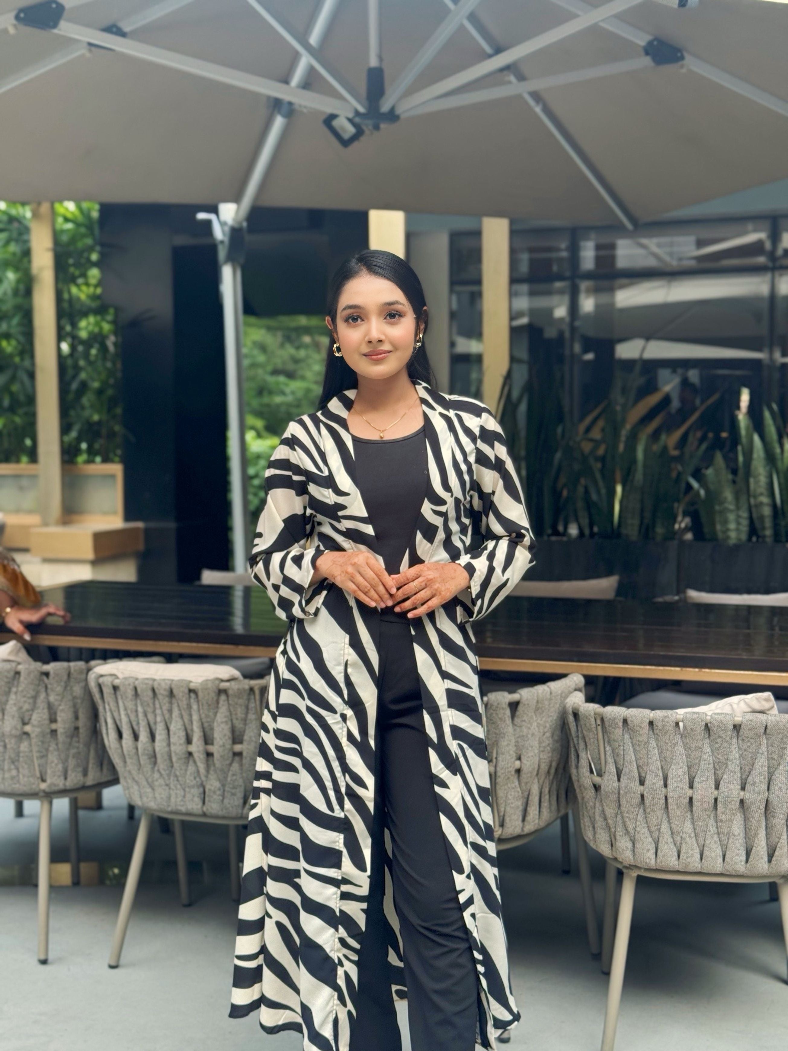 Woman wearing a zebra print long shrug in an outdoor setting with tables and chairs.