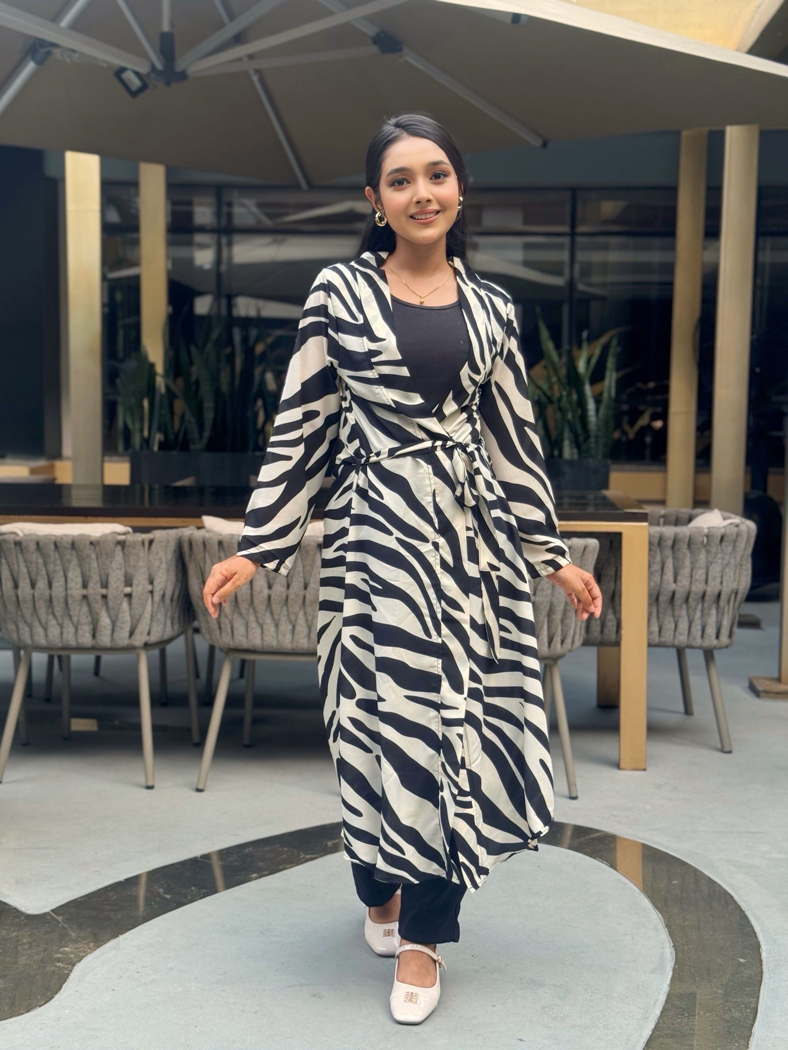 Woman wearing a zebra print long shrug in an indoor setting with tables and chairs.