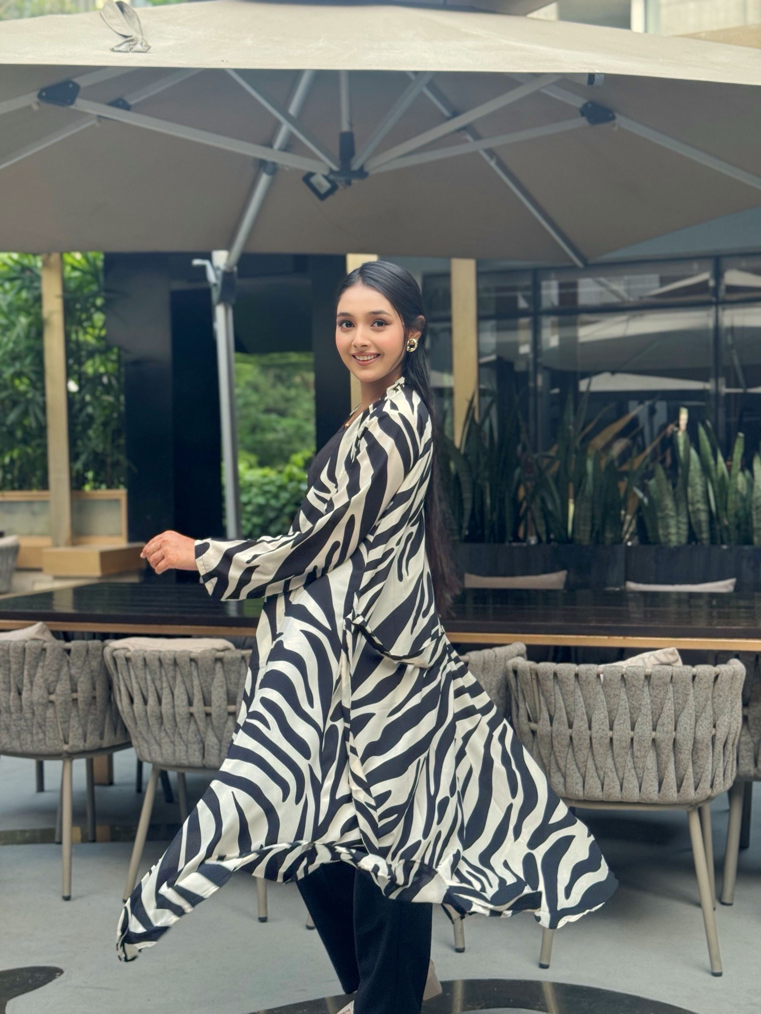 Woman in a zebra print long shrug standing outdoors under an umbrella.