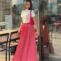 Woman in a white top and pink pleated skirt standing in front of a glass door.