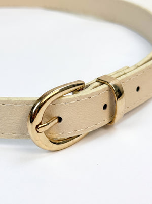 A close-up of a light beige leather belt with a polished gold-tone metal buckle, shown on a clean white background.