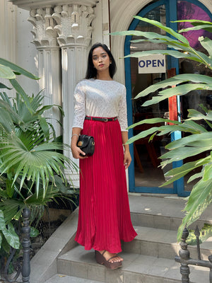 Woman in a white top and red skirt standing in front of a building entrance with plants around.