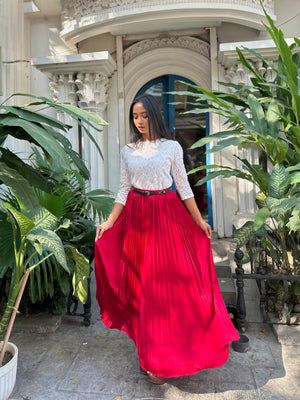 Woman in a white top and red skirt standing in front of a building with plants.