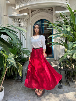 Woman in a white top and red skirt standing in front of a decorative building entrance with plants.