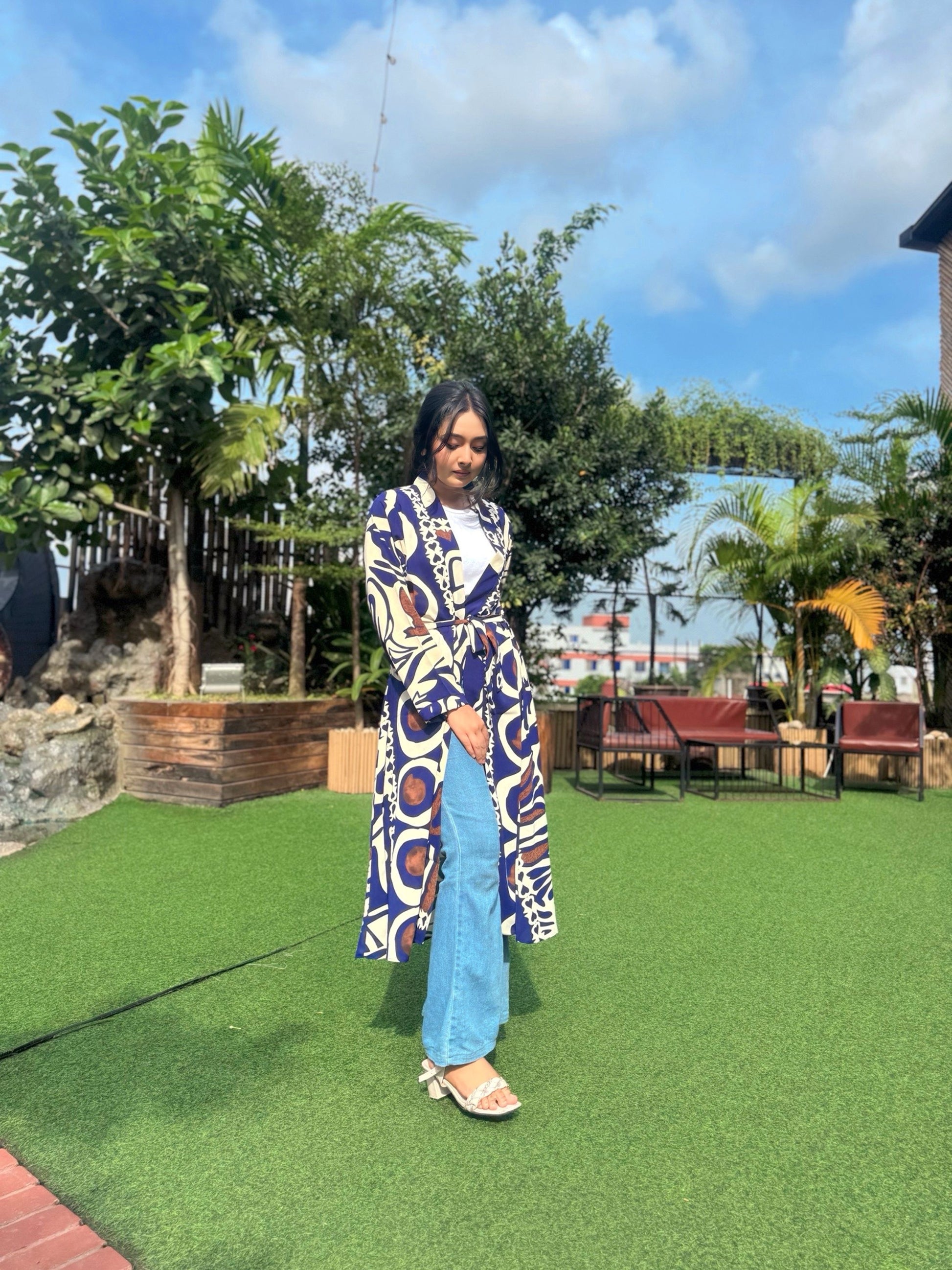 Woman wearing a long patterned shrug-style jacket and jeans with a handbag outdoors.