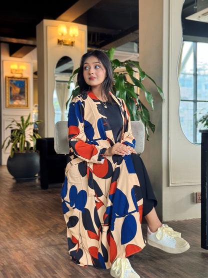 Woman in a colorful Long shrug standing in an indoor setting with plants and decor.