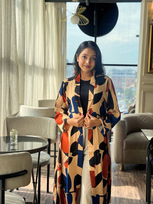 Woman in a patterned long shrug standing in a modern interior setting with large windows.