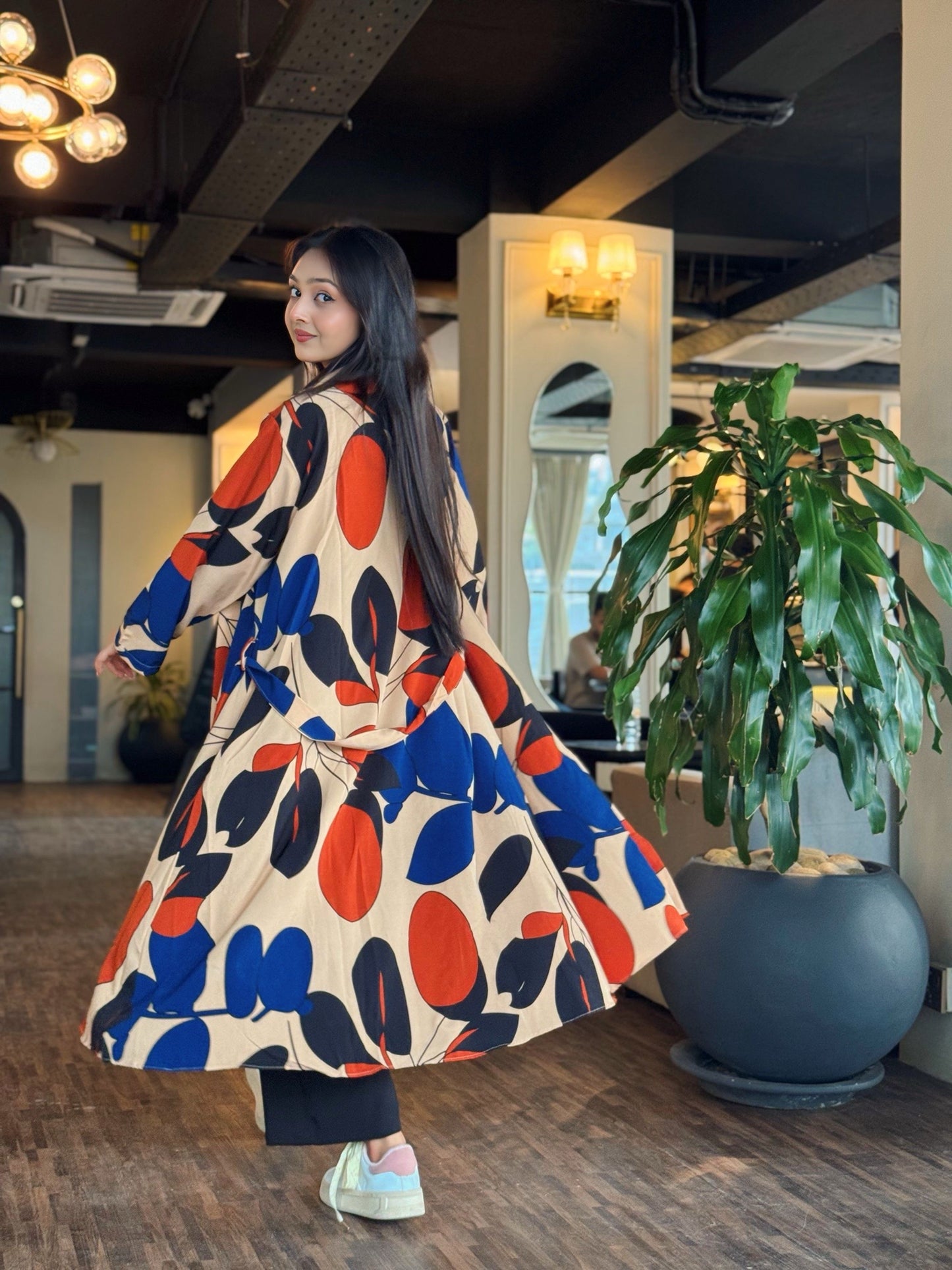 Woman in a colorful long shrug posing indoors with plants and decor in the background