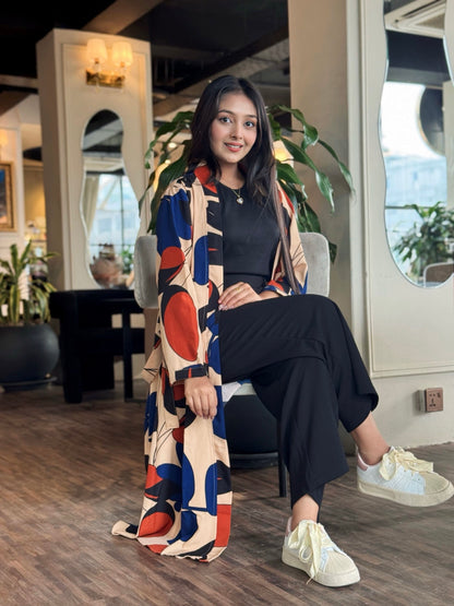 Woman sitting in a modern interior setting wearing a colorful patterned long shrug.