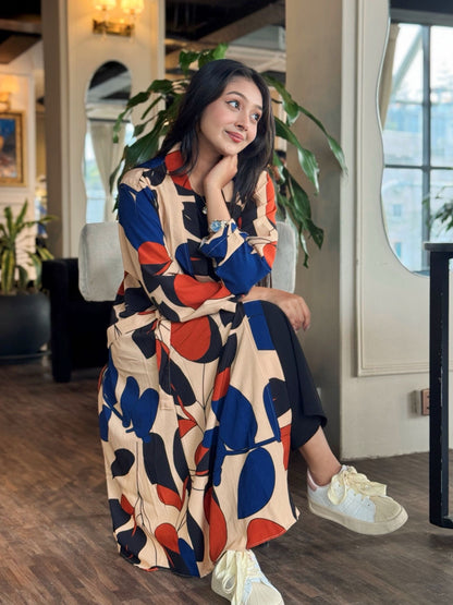 Woman in a colorful long shrug sitting indoors with plants and a window in the background