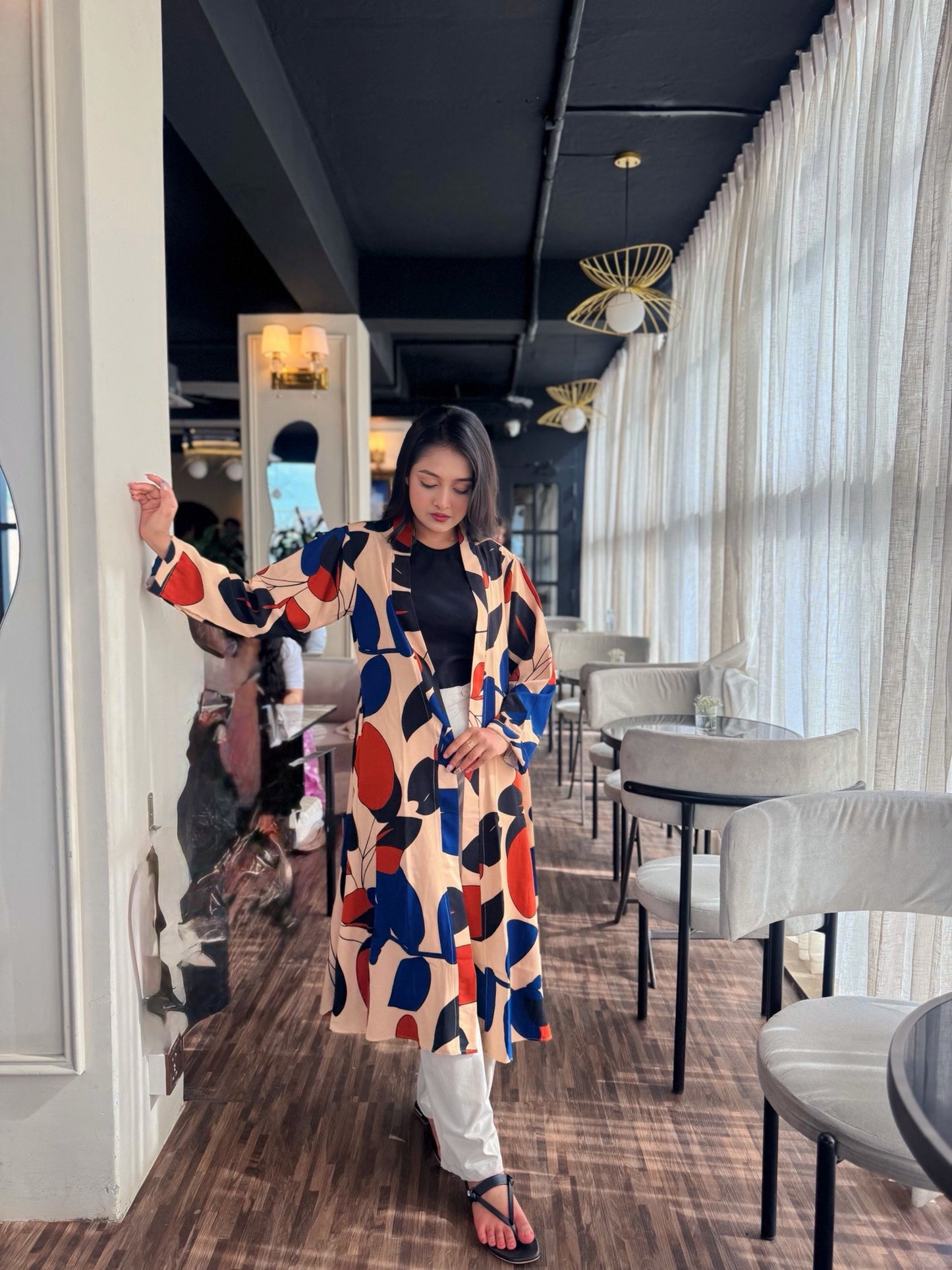 Woman in a colorful patterned long shrug standing in a modern restaurant.