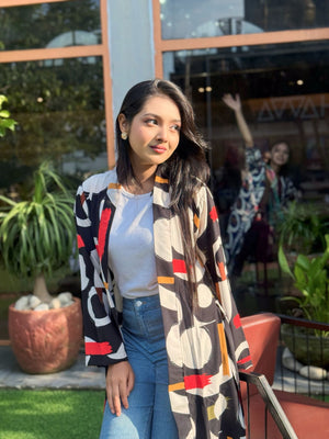 Woman wearing a colorful patterned long shrug outdoors with plants and a building in the background