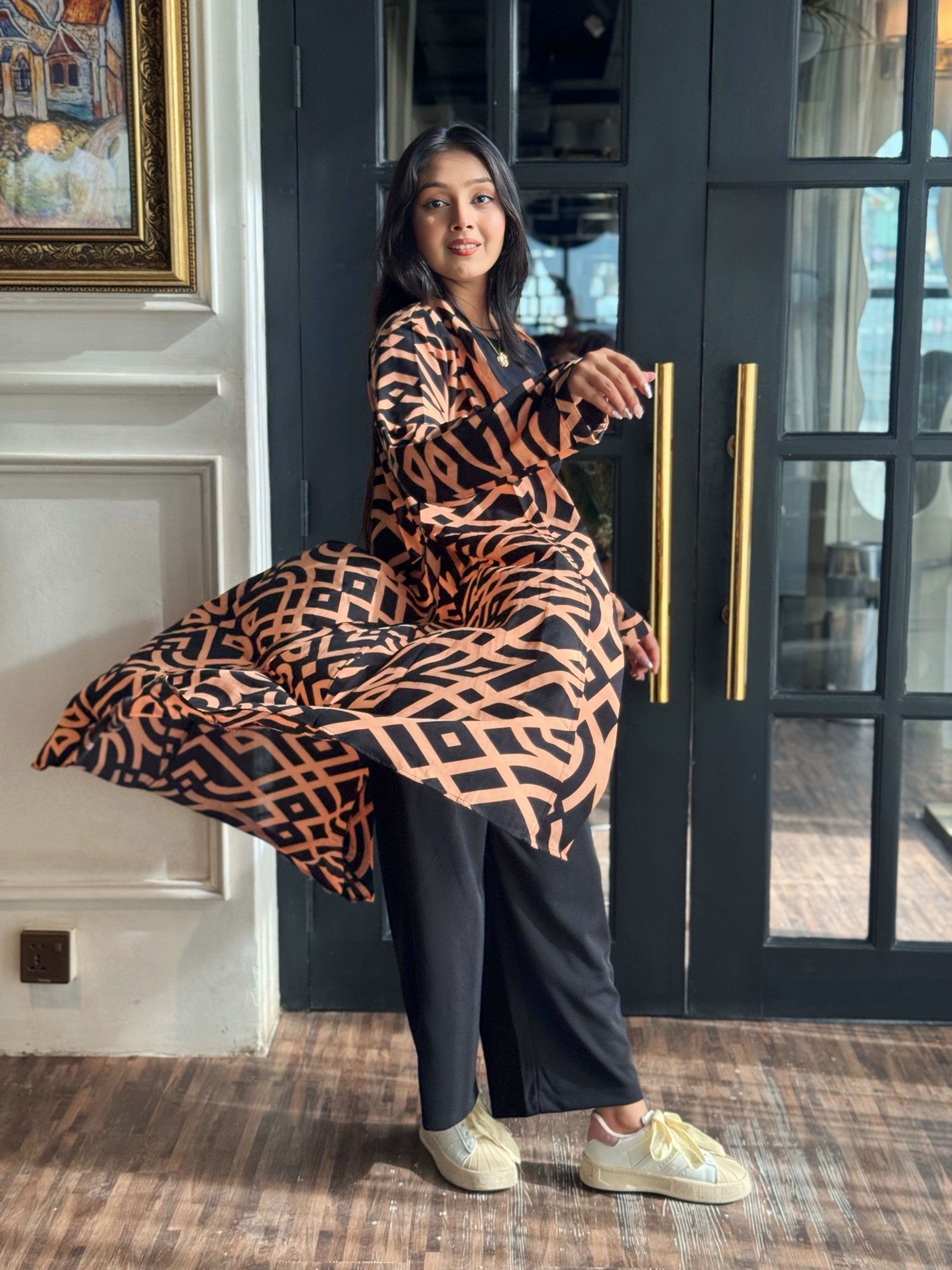 Woman wearing a Woman wearing a long shrug outerwear  in black and orange standing in front of a glass door.