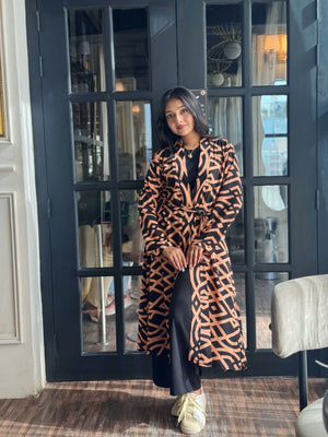 Woman wearing a Woman wearing a long shrug outerwear  in black and orange standing in front of a glass door.