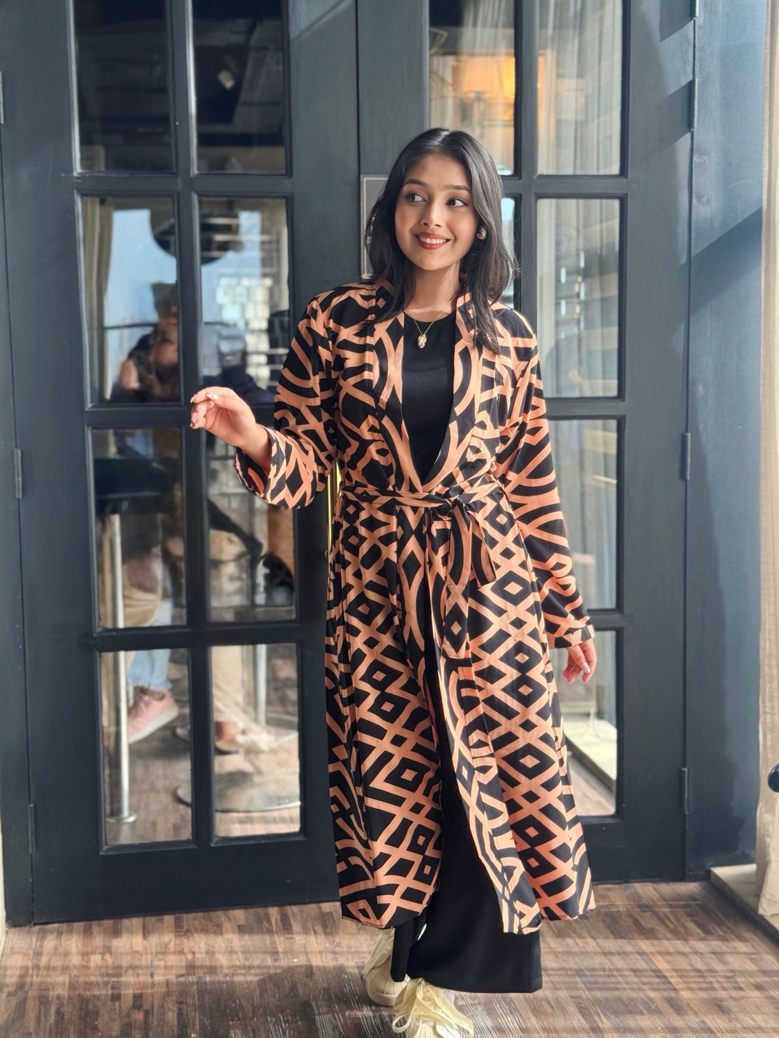 Woman wearing a Woman wearing a long shrug outerwear  in black and orange standing in front of a glass door.