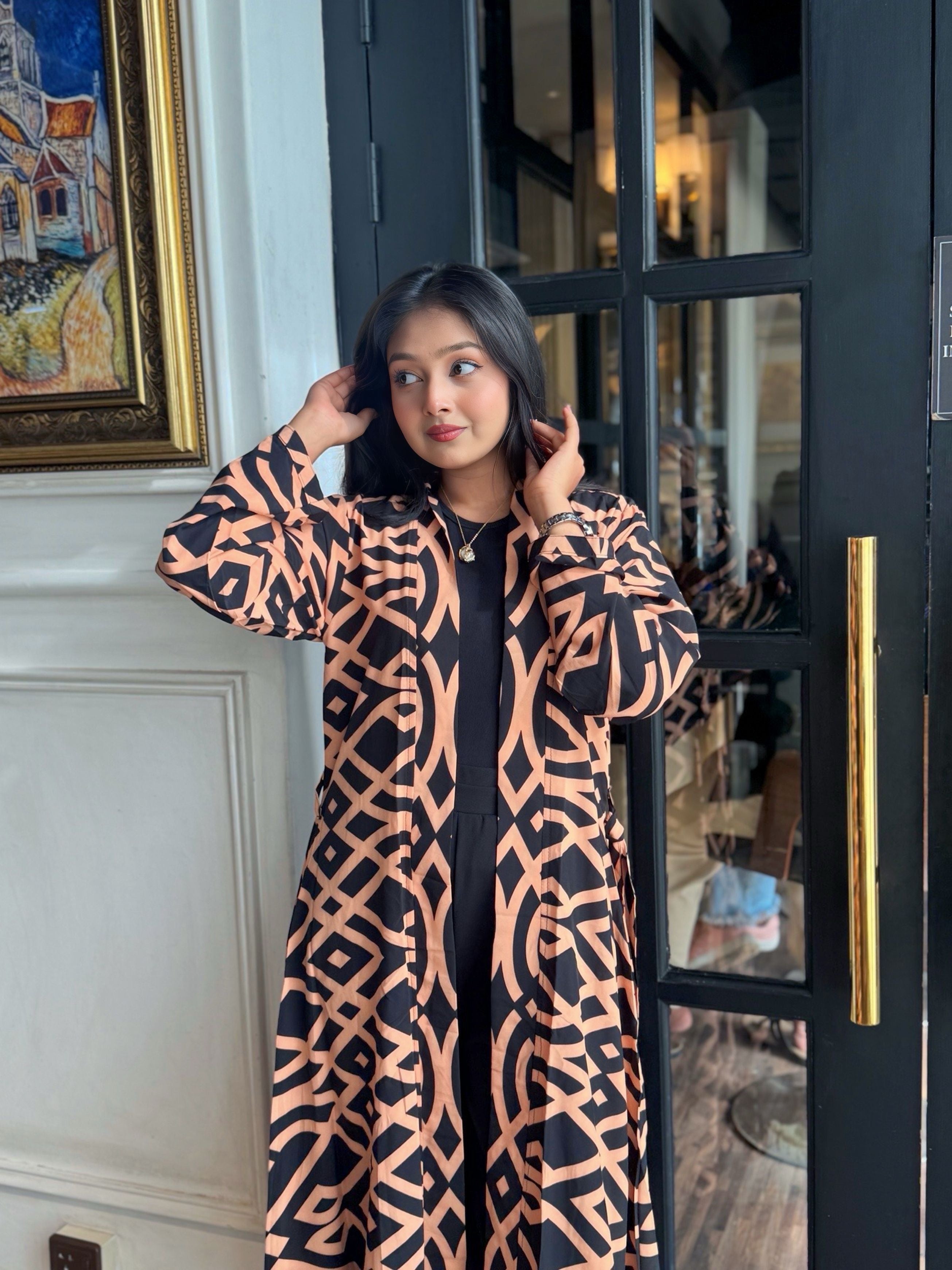 Woman wearing a long shrug outerwear  in black and orange standing in front of a door.