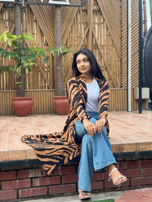 Woman wearing a tiger print long shrug and blue jeans sitting on a ledge with a bamboo background.