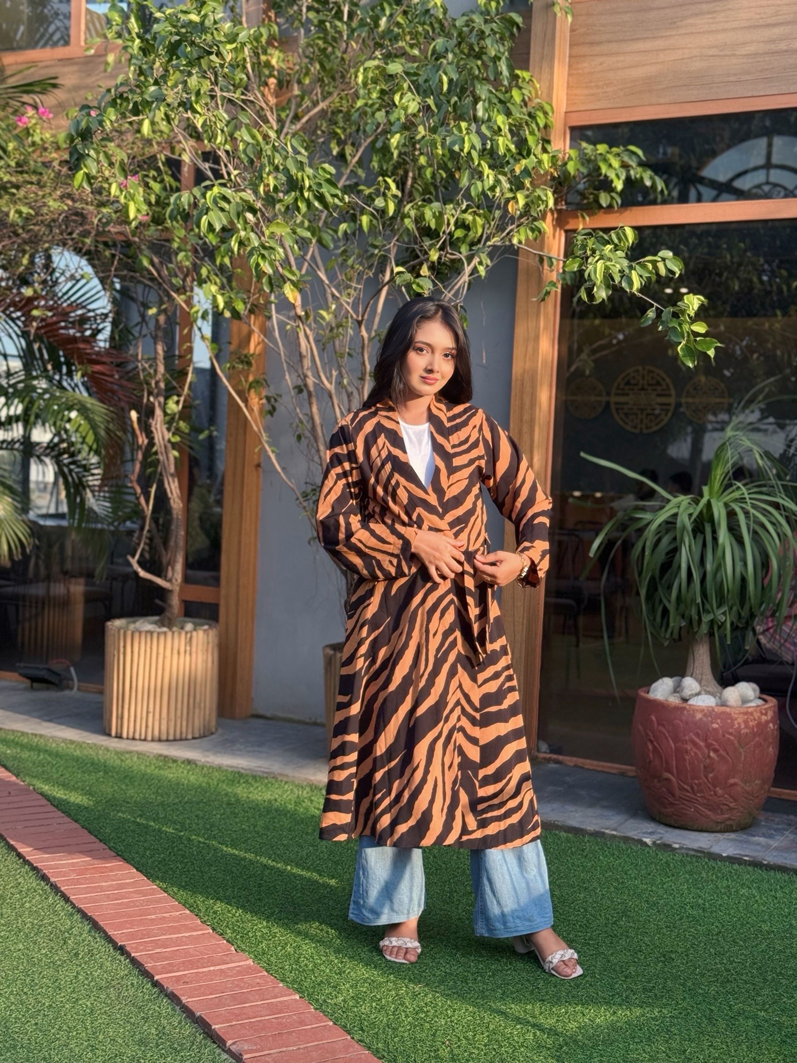 Woman wearing a tiger-striped long shrug standing outdoors with plants and a building in the background