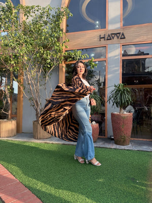 Woman wearing a long shrug on grass in front of a building with 'HAWA' branding