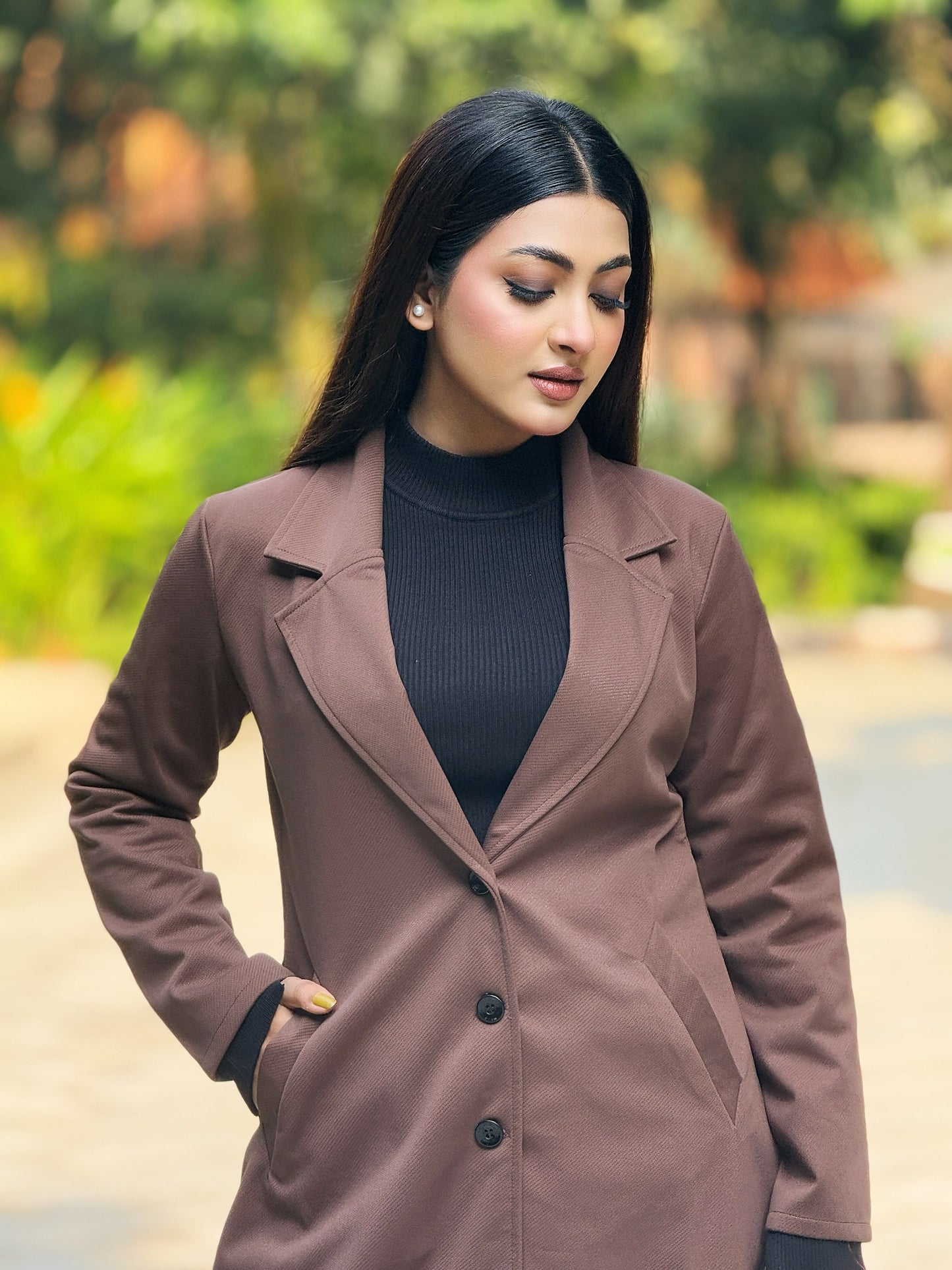 Woman wearing a brown coat with a blurred green outdoor background