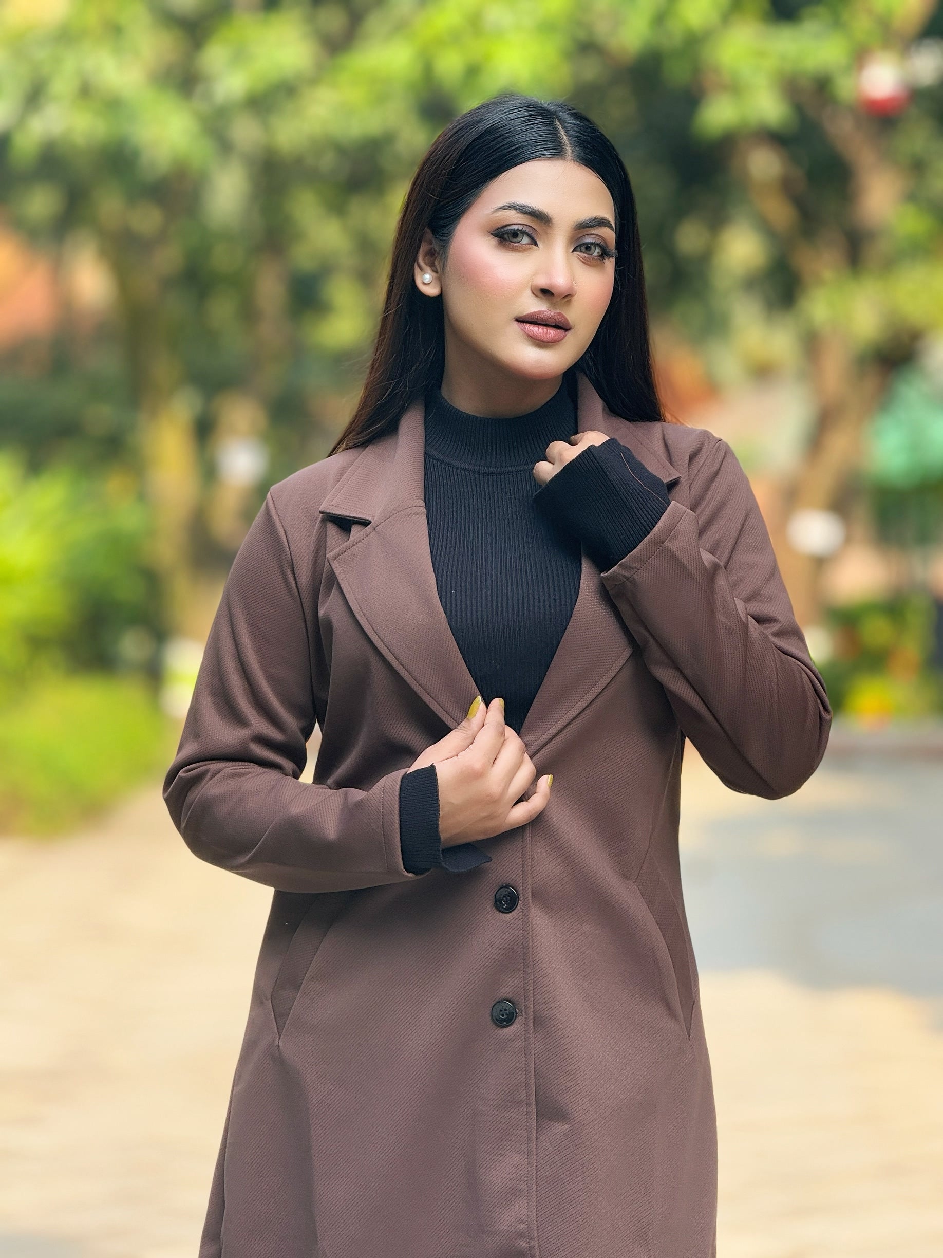 Woman wearing a brown coat over a black turtleneck in an outdoor setting