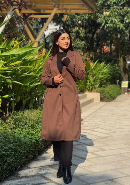 Woman in a brown coat walking on a path with greenery around