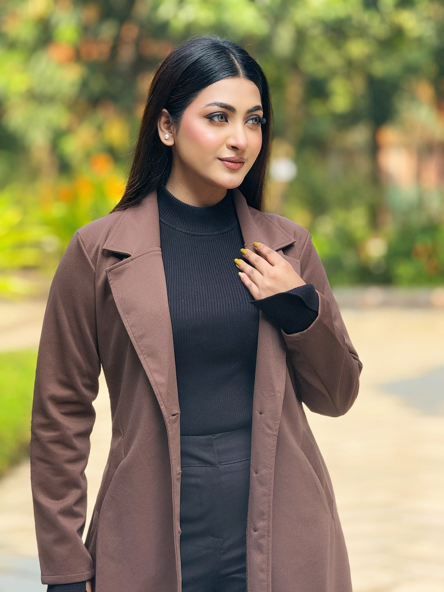 Woman wearing a brown coat over a black outfit with a blurred green background