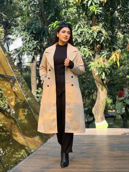 Woman in a beige coat walking on a wooden path with greenery in the background