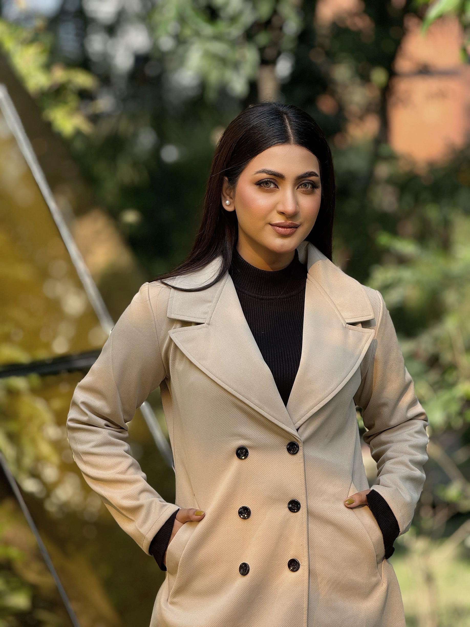 Woman wearing a beige trench coat with a blurred natural background