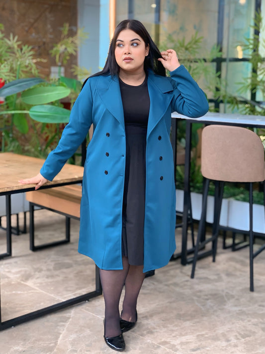 Woman wearing a blue coat in an outdoor setting with plants and tables.