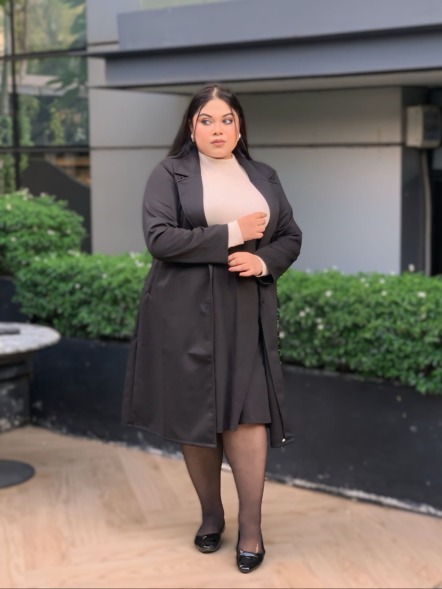 Woman wearing a black coat standing in front of a modern building.