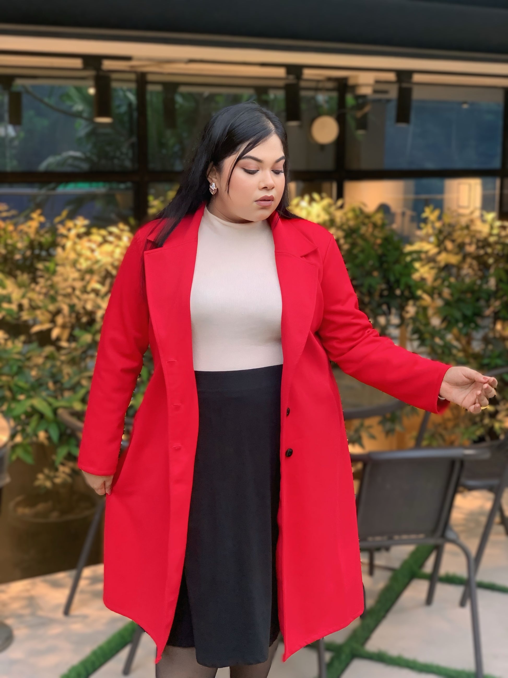 Woman wearing a red coat over a beige top and black skirt, standing outdoors.