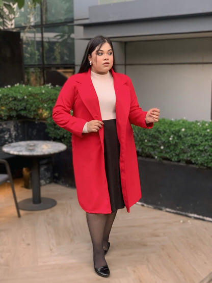 Woman wearing a red coat standing outdoors with greenery and a building in the background