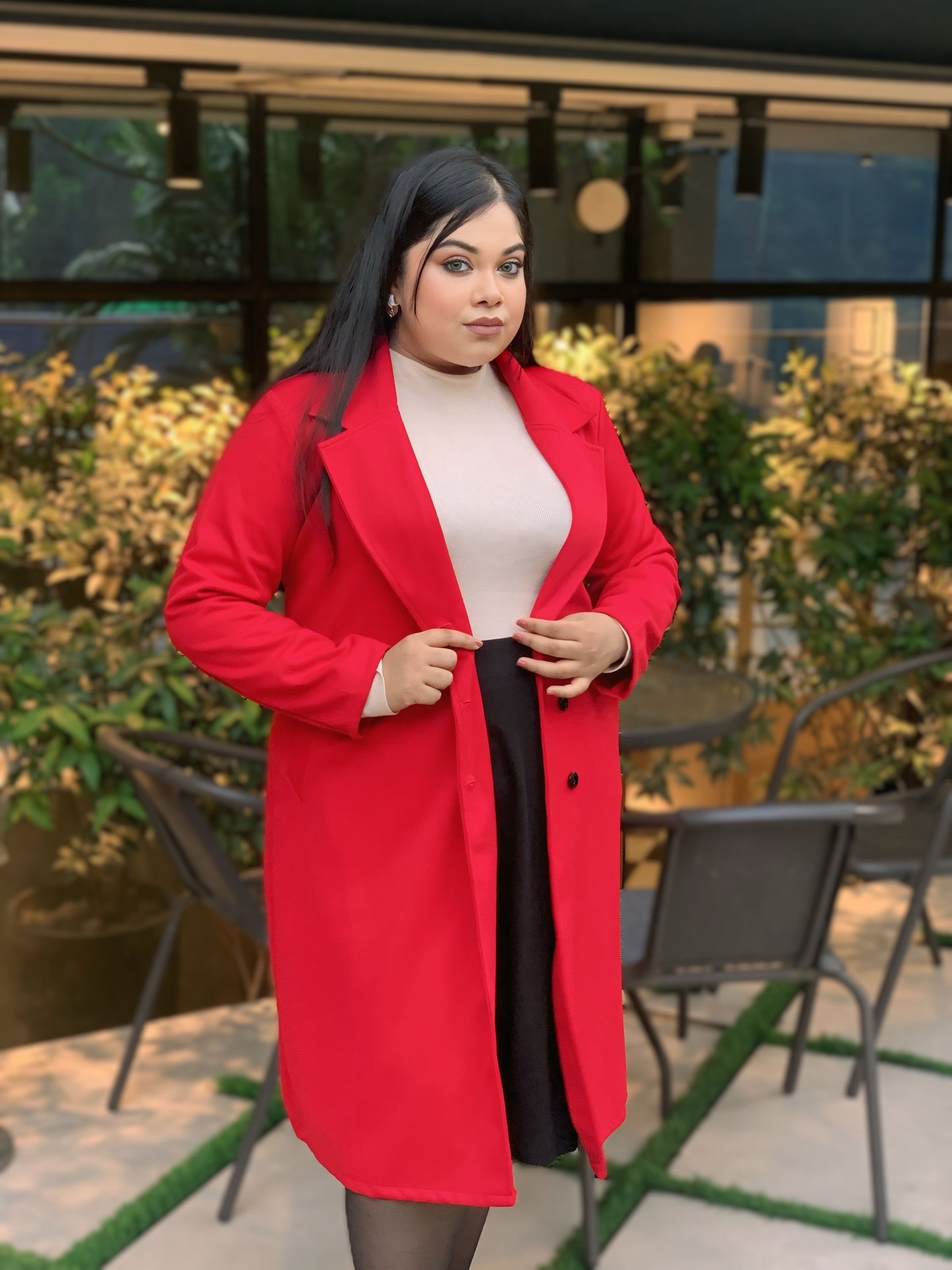 Woman wearing a red coat outdoors with greenery in the background